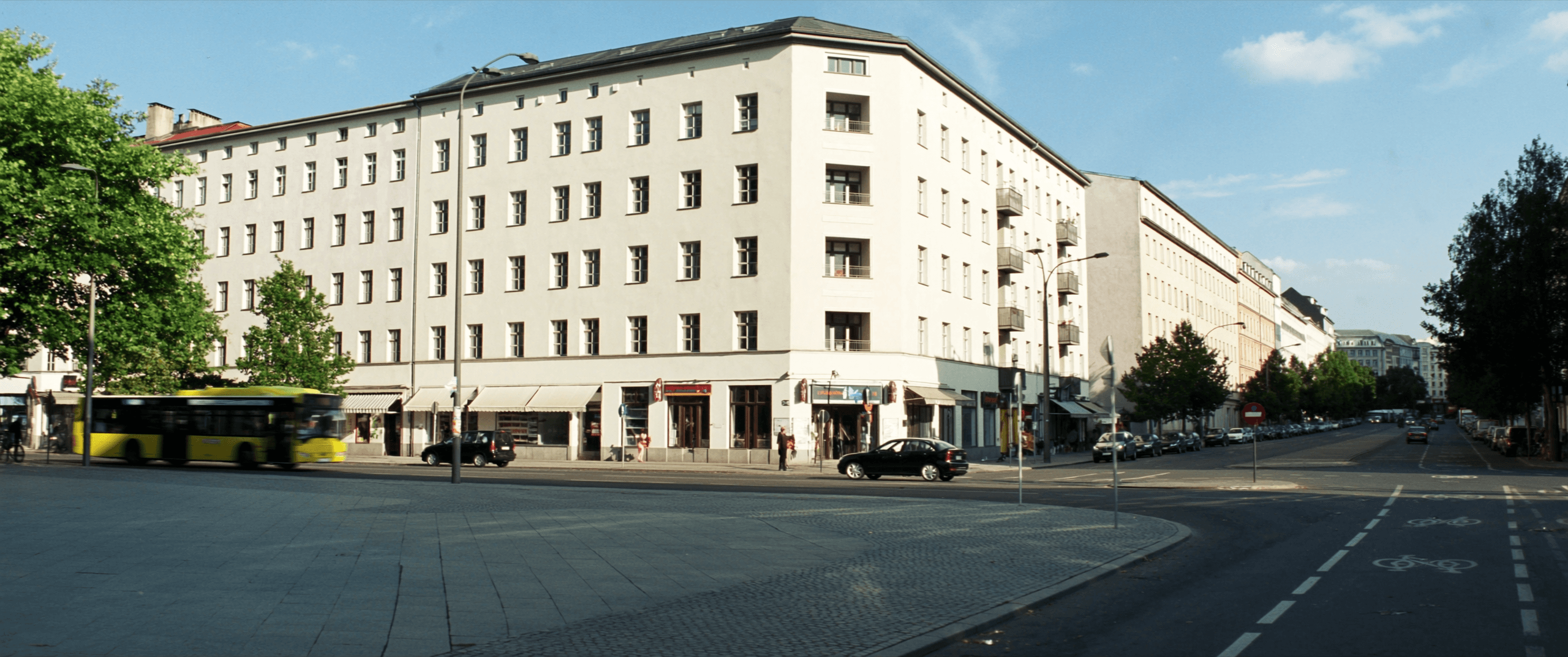 Straßenzug im Berliner Bezirk Wedding mit Altbauten, Geschäften und einem gelben Bus.